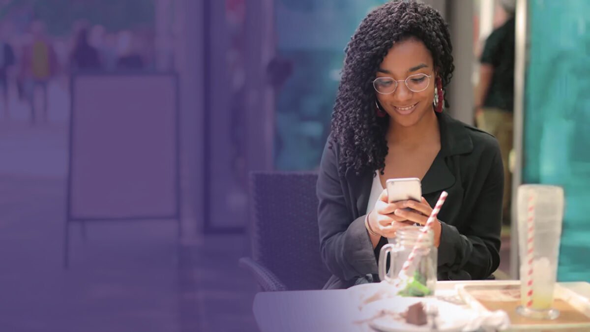 A young woman in glasses using her smartphone at an outdoor café table with a drink and food, reviewing an SQF template.