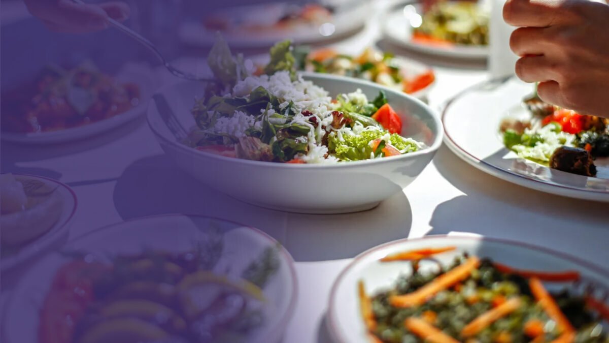 A person's hand serving a mixed salad onto a plate from a buffet of various dishes, prepared according to SQF program standards.